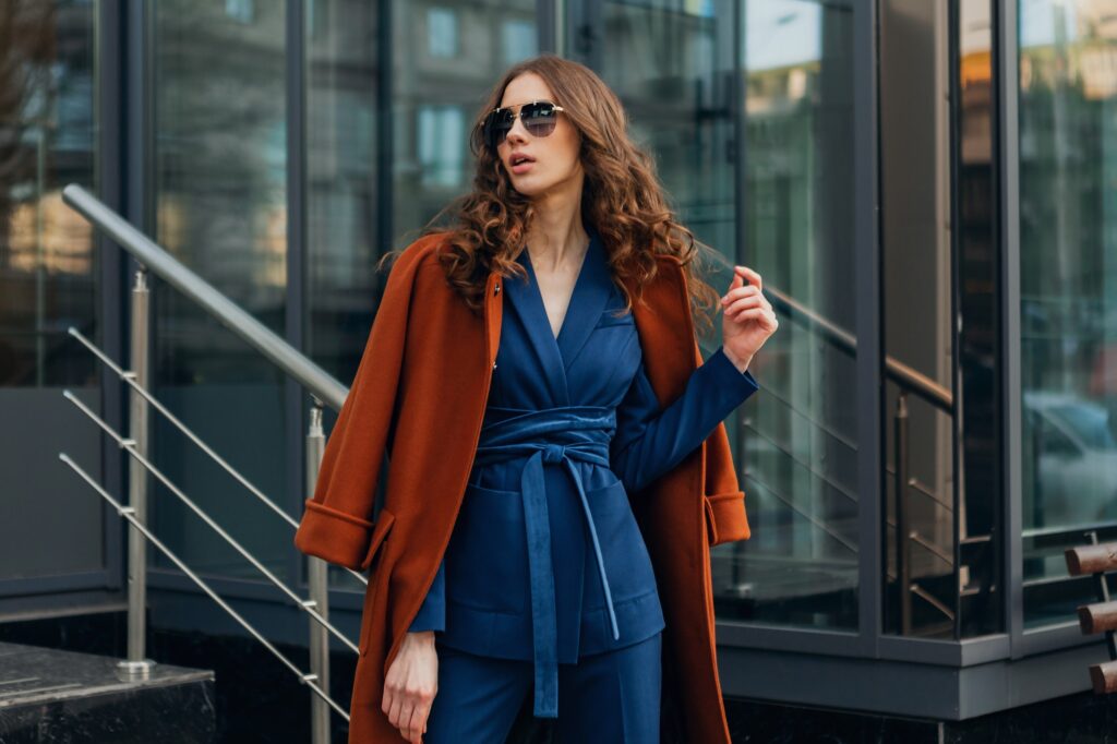 beautiful stylish woman walking in street stairs dressed in warm brown coat and blue suit