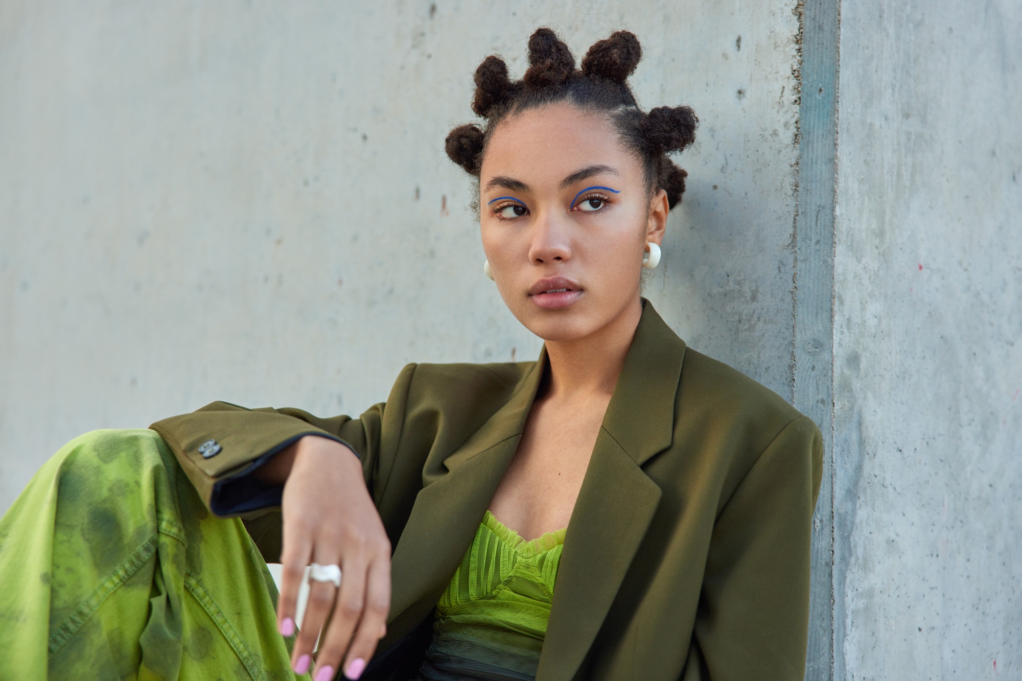 Photo of serious young woman with bun hairstyle has blue eyeliner dressed in fashionable clothes con